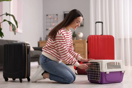 Lächelnde Frau bereitet sich darauf vor, mit Hund im Haus zu reisen. Koffer und Haustierhalter um sie herum