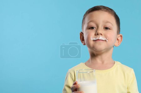 Téléchargez les photos : Garçon mignon avec moustache au lait tenant un verre de boisson laitière savoureuse sur fond bleu clair, espace pour le texte - en image libre de droit