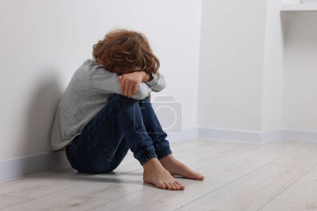 Kindesmissbrauch. Aufgebrachter Junge sitzt auf dem Boden neben weißer Wand, Platz für Text