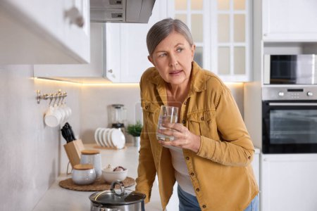 Menopause. Woman with glass of water suffering from hot flash in kitchen