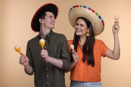 Téléchargez les photos : Belle femme de couple en sombrero mexicain chapeaux avec des maracas sur fond beige - en image libre de droit