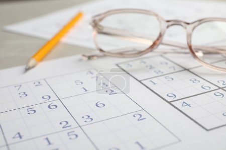 Foto de Sudoku, lápiz y anteojos en la mesa, vista de cerca - Imagen libre de derechos