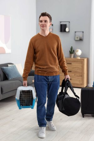 Téléchargez les photos : Voyage avec animal de compagnie. Homme tenant transporteur avec chat mignon et sac à la maison - en image libre de droit
