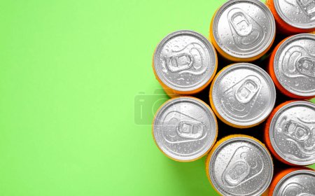Energy drinks in wet cans on green background, top view. Space for text