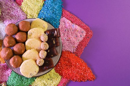 Diwali-Feier. Leckere indische Süßigkeiten und bunte Rangoli auf violettem Hintergrund, flache Lage. Raum für Text