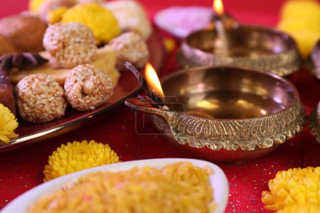 Téléchargez les photos : Fête de Diwali. Lampes Diya et savoureux bonbons indiens sur table rouge brillant, gros plan - en image libre de droit