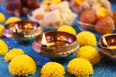 Téléchargez les photos : Fête de Diwali. Lampe Diya et fleurs de chrysanthème sur table bleu clair brillant, gros plan - en image libre de droit