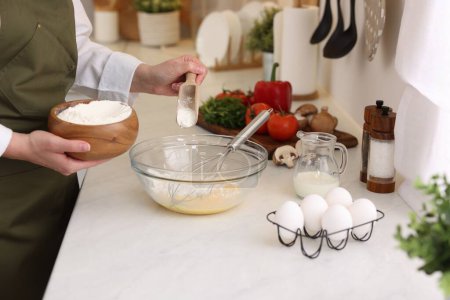 Woman adding flour into bowl at light table, closeup
