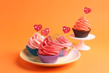Delicious cupcakes with bright cream and heart toppers on orange background