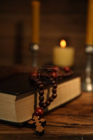 Photo for Cross, Bible, rosary beads and church candles on wooden table, closeup - Royalty Free Image
