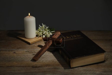 Cruz, Biblia, vela de iglesia y flores sobre mesa de madera