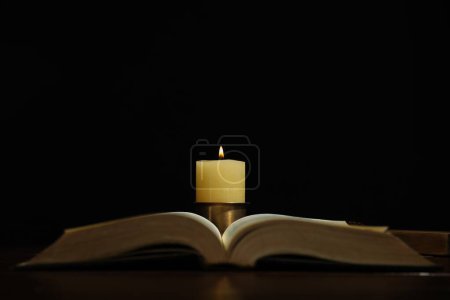 Church candle and Bible on table against black background