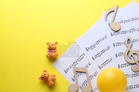 Babylieder. Notenblätter, Holznotizen, Spielzeugbären und Ball auf gelbem Hintergrund, Draufsicht mit Platz für Text