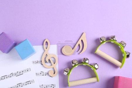 Werkzeuge zum Erstellen von Babyliedern. Flache Komposition mit hölzernen Noten und Tamburinen für Kinder auf violettem Hintergrund
