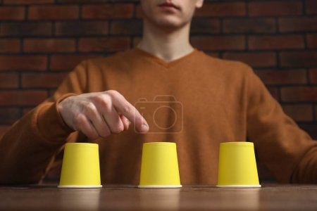 Man playing shell game at wooden table, low angle view