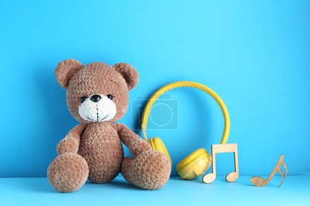 Babylieder. Spielzeugbär, gelbe Kopfhörer und Holznotizen auf hellblauem Hintergrund