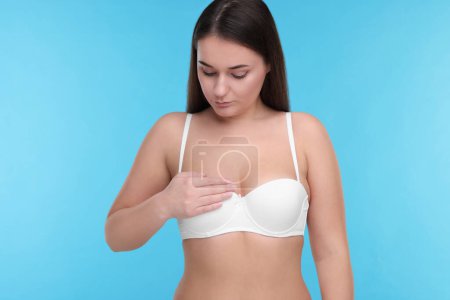 Mammology. Woman in bra doing breast self-examination on light blue background
