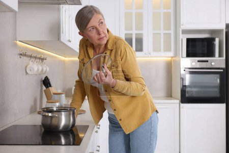 Menopause. Woman suffering from hot flash while cooking in kitchen