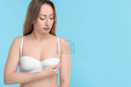 Mammology. Young woman doing breast self-examination on light blue background, space for text
