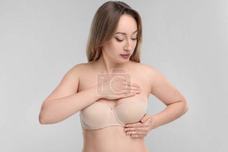 Mammology. Young woman doing breast self-examination on light grey background