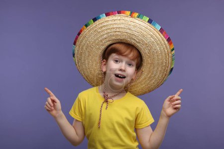 Chico sorprendido con sombrero mexicano señalando algo sobre fondo violeta