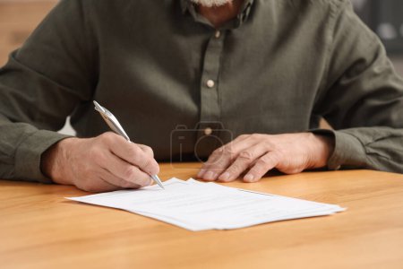 Foto de Hombre mayor firmando Última Voluntad y Testamento en mesa de madera en el interior, primer plano - Imagen libre de derechos