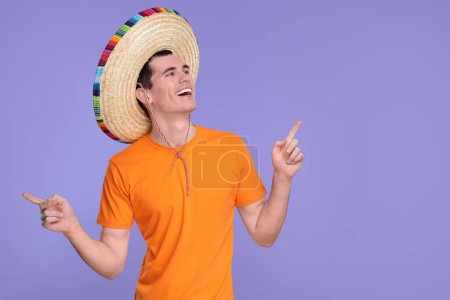 Un joven con sombrero mexicano señalando algo sobre fondo violeta. Espacio para texto