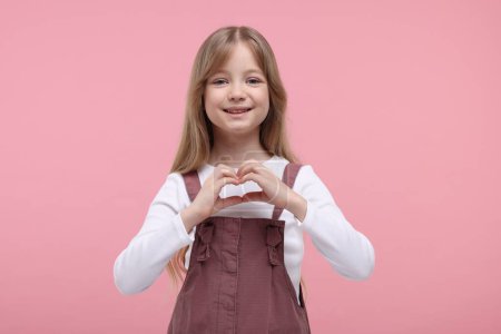Glückliches Mädchen zeigt Herz-Geste mit Händen auf rosa Hintergrund