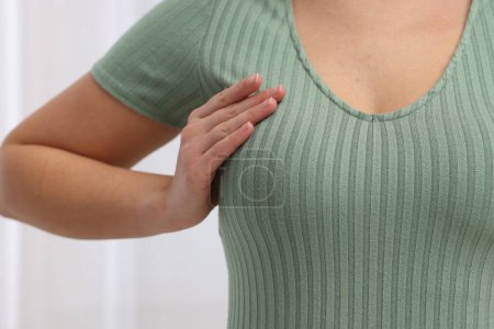 Mammology. Woman doing breast self-examination indoors, closeup