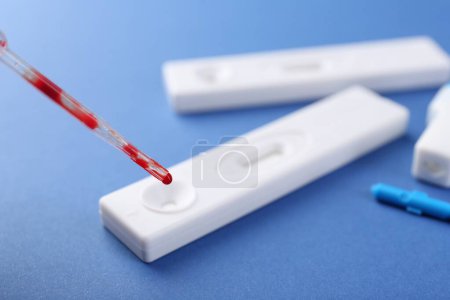 Dropping blood sample onto disposable express test cassette with pipette on blue background, closeup
