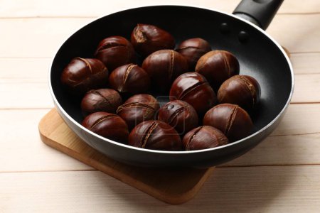 Roasted edible sweet chestnuts in frying pan on wooden table
