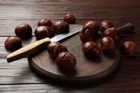 Roasted edible sweet chestnuts and knife on wooden table, closeup