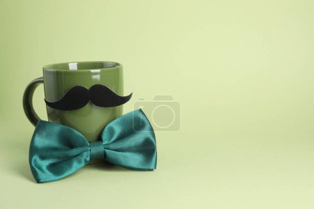 Téléchargez les photos : Visage d'homme fait de tasse, fausse moustache et noeud papillon sur fond vert clair. Espace pour le texte - en image libre de droit
