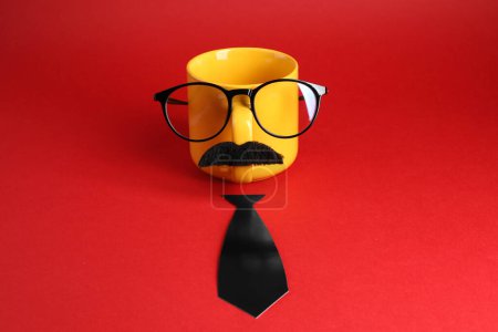 Téléchargez les photos : Visage d'homme en tasse, fausse moustache, lunettes et cravate en papier sur fond rouge - en image libre de droit