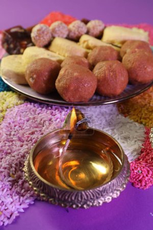 Diwali-Feier. Leckere indische Süßigkeiten, Diya-Lampe und bunte Rangoli auf violettem Tisch, Nahaufnahme