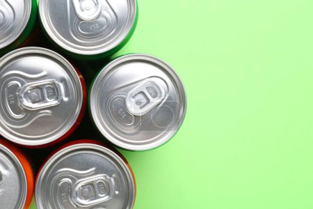 Bebida energética en latas sobre fondo verde claro, vista superior. Espacio para texto