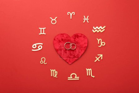 Foto de Signos del zodíaco, corazón y anillos de boda sobre fondo rojo, cama plana - Imagen libre de derechos