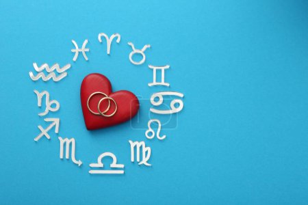 Zodiac signs, heart and wedding rings on light blue background, flat lay. Space for text