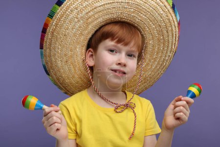 Lindo chico en sombrero mexicano con maracas sobre fondo violeta