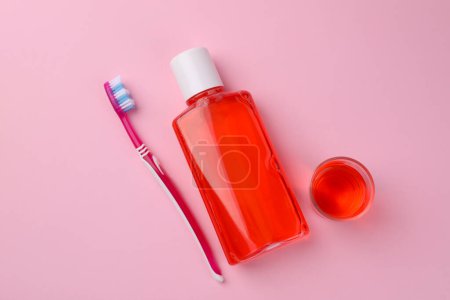 Foto de Enjuague bucal fresco en botella, vidrio y cepillo de dientes sobre fondo rosa, plano - Imagen libre de derechos