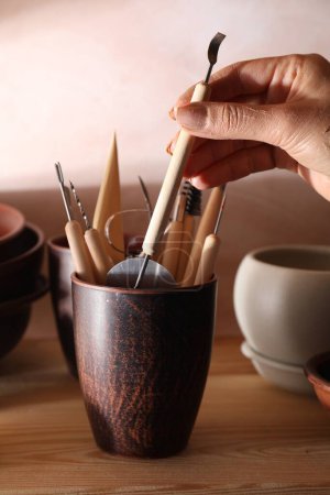 Woman taking clay crafting tool from cup in workshop, closeup