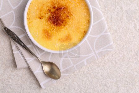 Photo for Delicious creme brulee in bowl and spoon on light textured table, top view. Space for text - Royalty Free Image