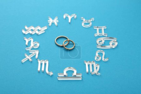 Zodiac signs and wedding rings on light blue background, closeup