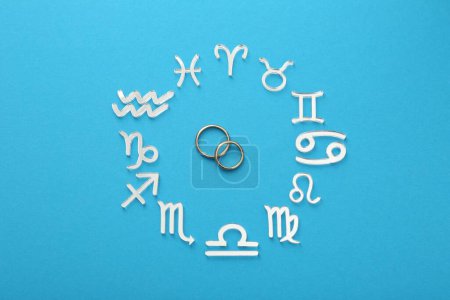 Zodiac signs and wedding rings on light blue background, flat lay