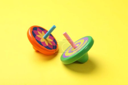 Two colorful spinning tops on yellow background, closeup