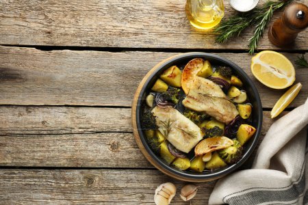 Foto de Trozos de delicioso bacalao al horno con verduras, limón y especias en plato sobre mesa de madera, puesta plana. Espacio para texto - Imagen libre de derechos