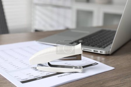 Stapler and document on wooden table indoors, closeup