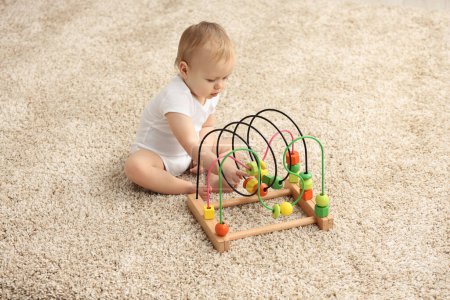 Kinderspielzeug. Niedlicher kleiner Junge spielt mit Perlen-Labyrinth auf Teppich zu Hause