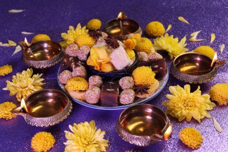 Téléchargez les photos : Fête de Diwali. Lampes Diya, bonbons indiens savoureux et fleurs de chrysanthème sur table violette brillante - en image libre de droit