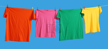 Bunte T-Shirts, die auf der Wäscheleine vor hellblauem Hintergrund trocknen, Banner-Design